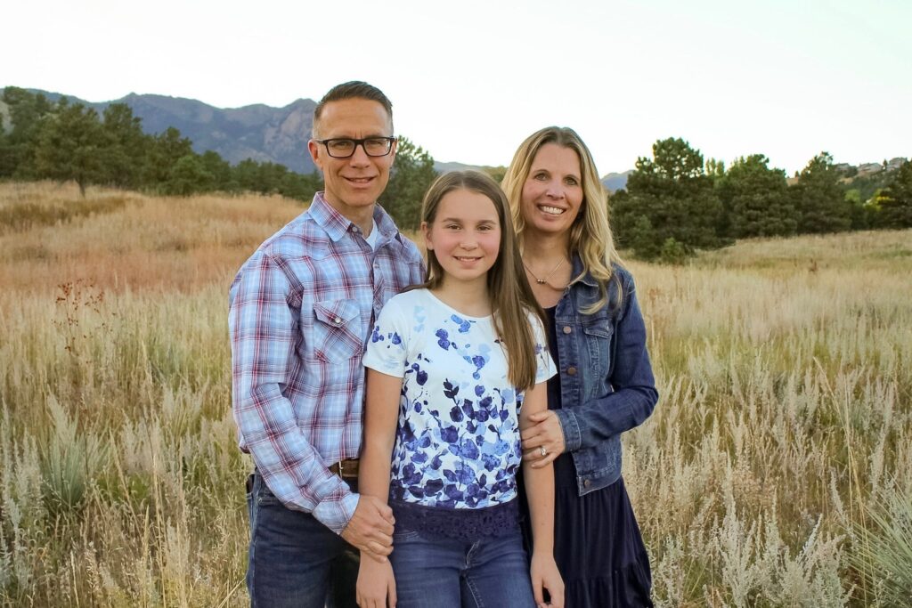 A smiling family standing together in front of a house.