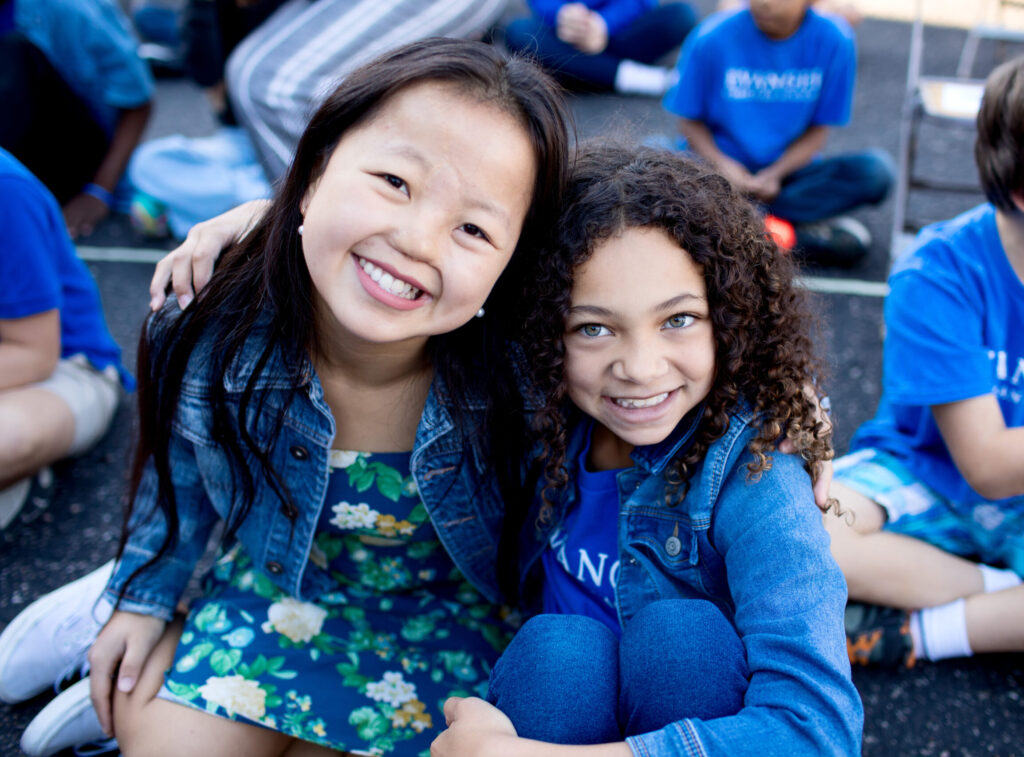 A middle school girl and an elementary aged girl hugging.