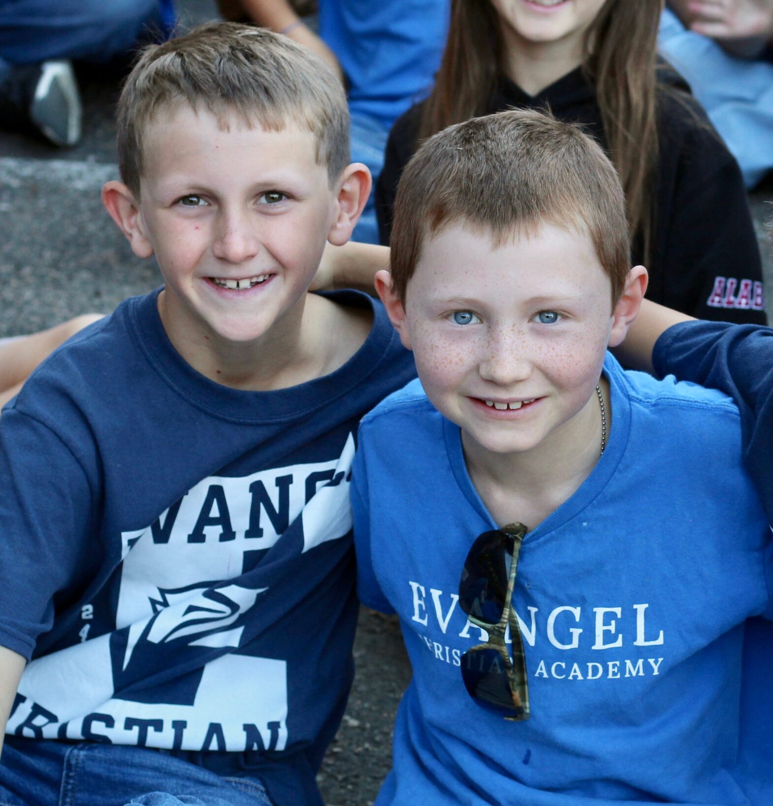 Two young boys with their arms around each other, at an outside school gathering